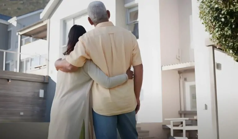 A senior couple stands in front of their new home
