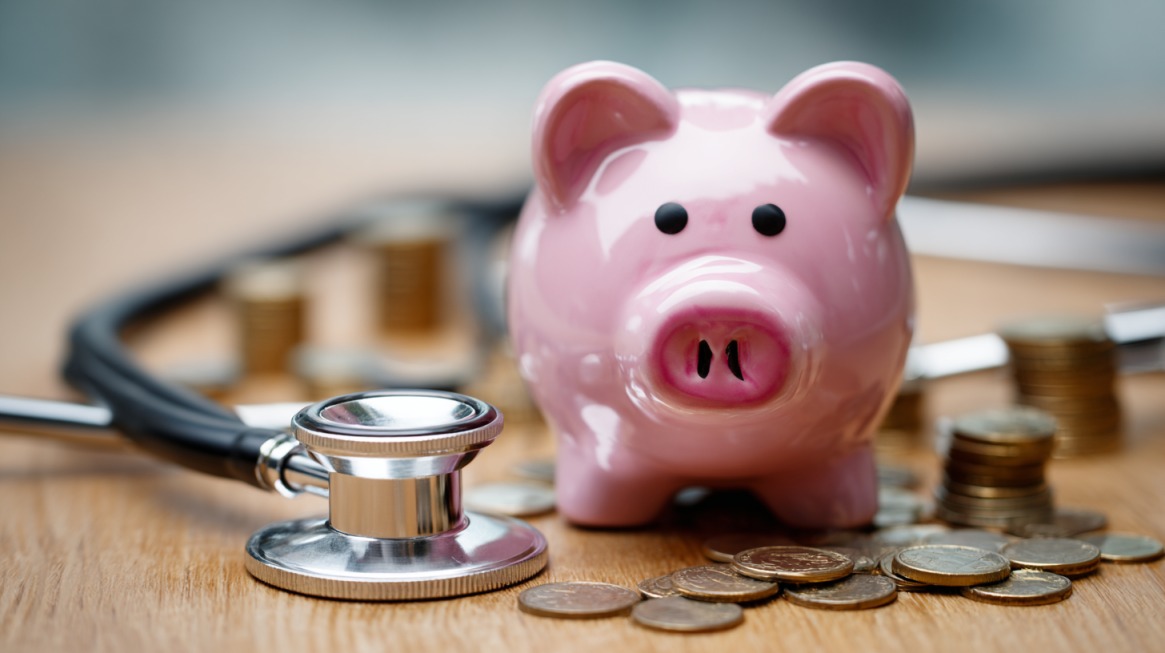 Pink piggy bank next to a stethoscope and stacked coins symbolizing healthcare expenses