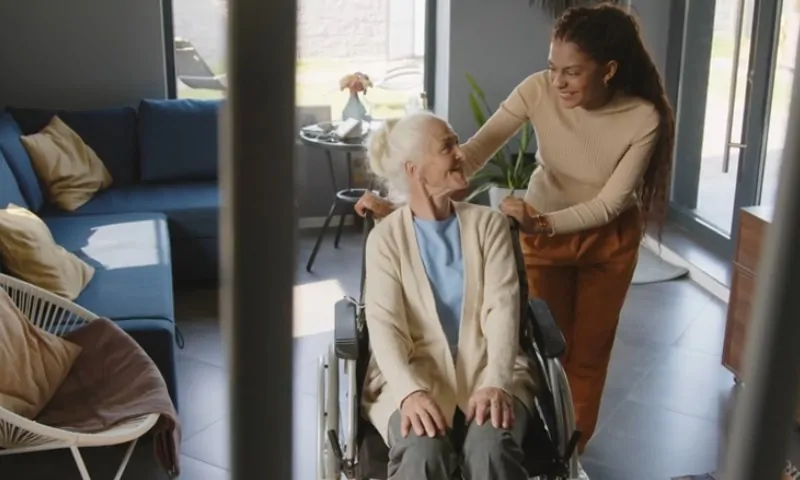 A woman in a wheelchair smiles at a standing woman who gently touches her shoulders