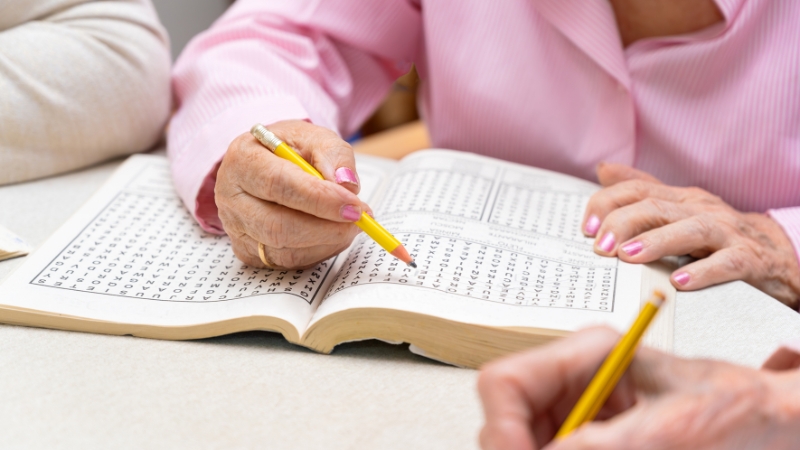 Seniors use pencils to solve a trivia-style puzzle together in a workbook