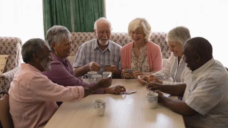 Seniors play trivia games together and focus on cards while chatting around a table