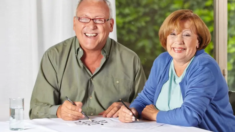 Older couple smiles while working together on a trivia sheet at a table