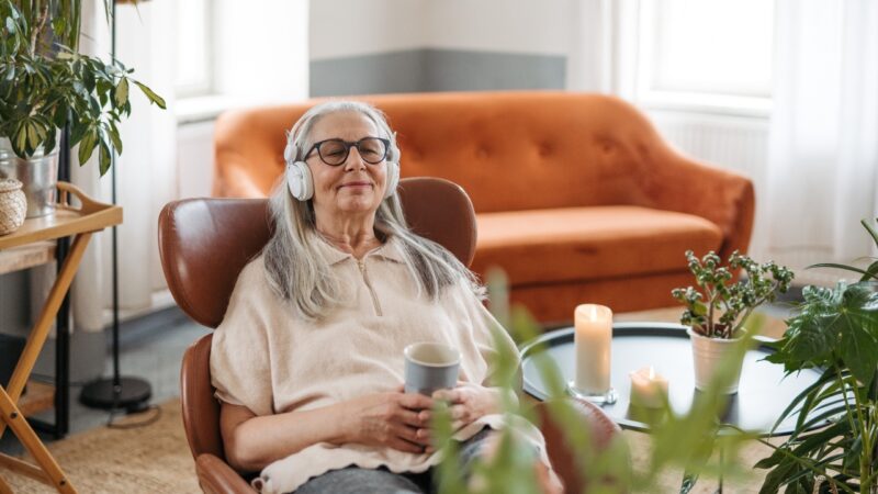 Older woman sitting in a chair at home listening to music with headphones