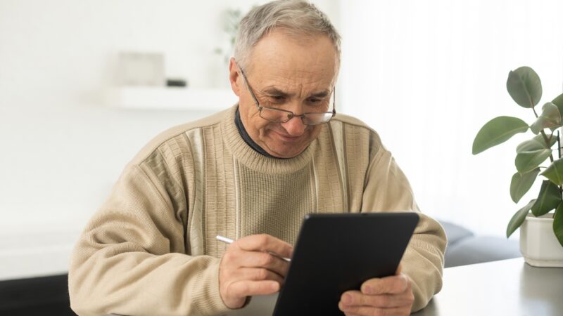 Older man using a tablet at home for reading or audiobooks