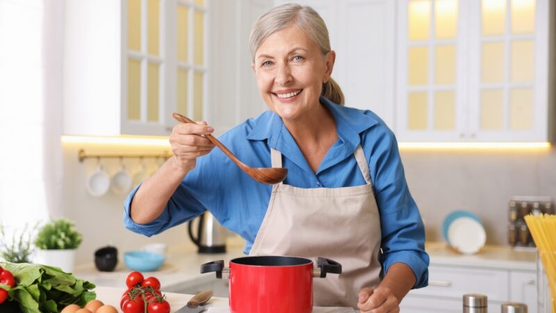 Older woman cooking at home and tasting food with a spoon