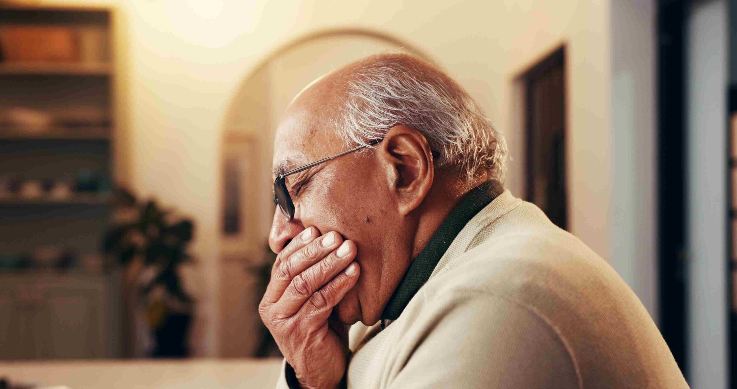 Elderly man holding his mouth while experiencing discomfort at home