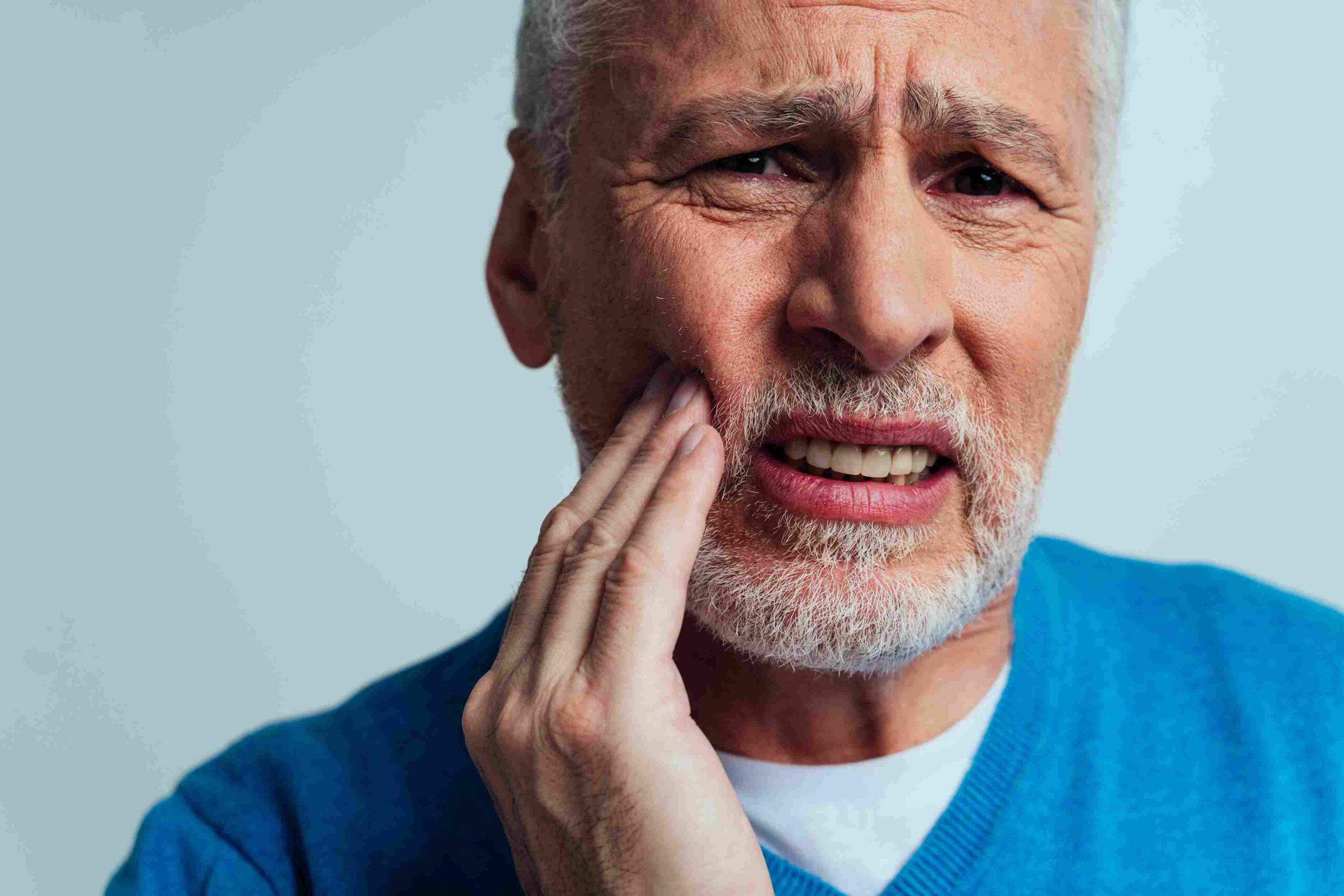 Senior man holding his cheek while experiencing denture or tooth pain