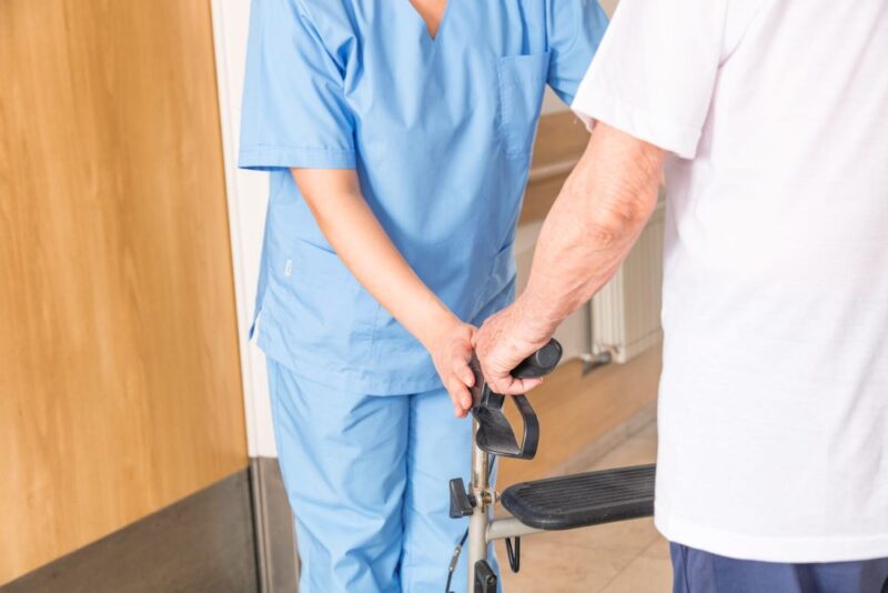 Nurse helping elderly man with walker in hospital.