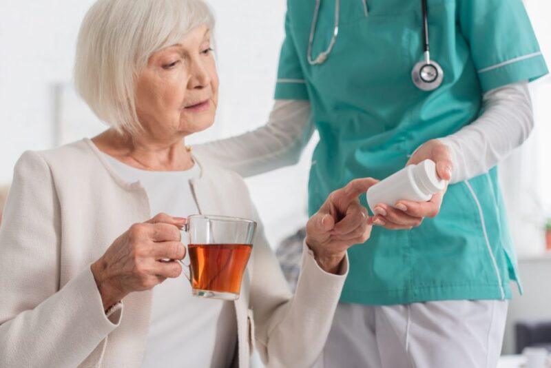 Caregiver helping an older woman with medication in her kitchen