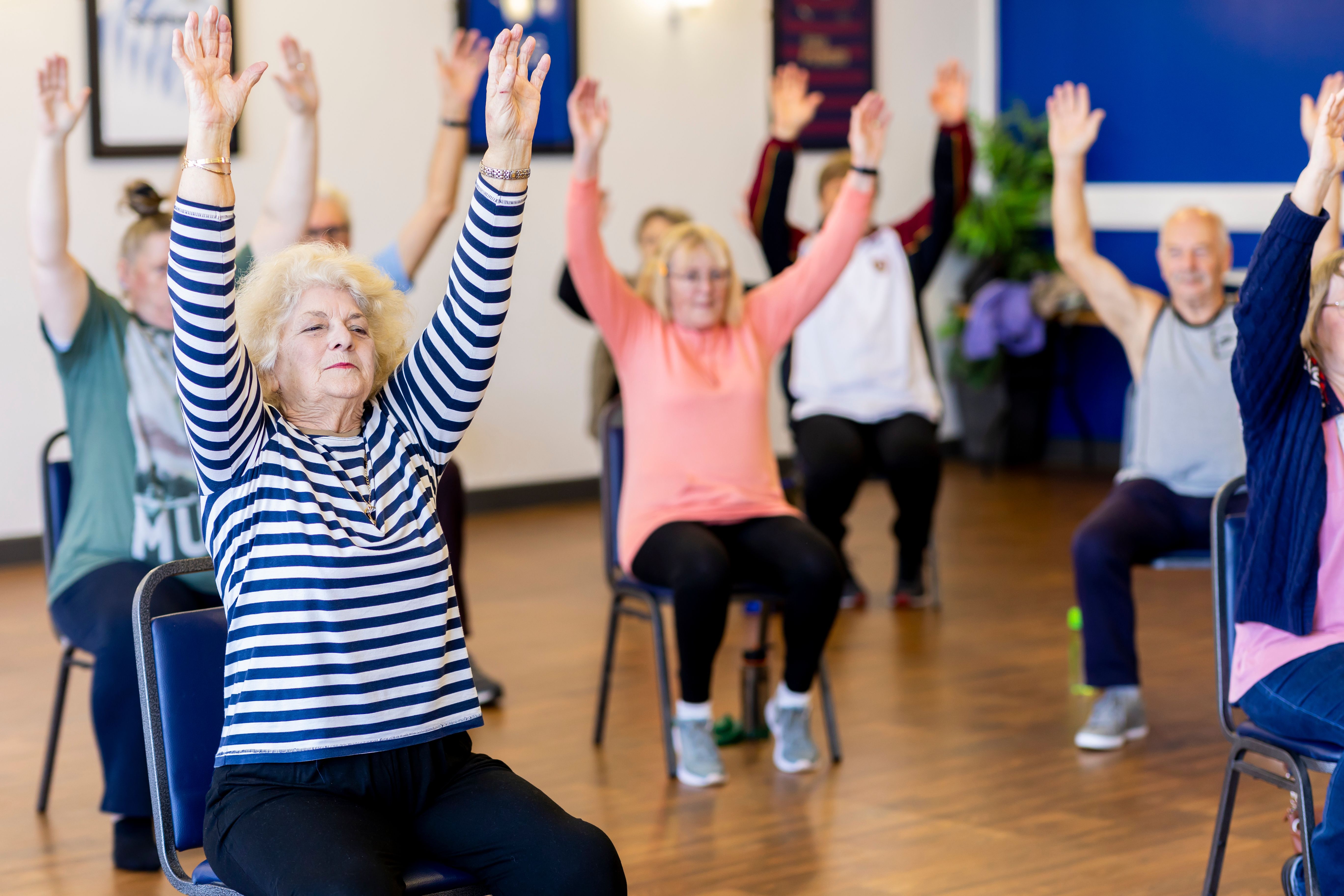 A group of older adults participate in a seated exercise class at a community center.