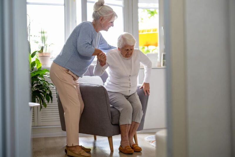 Caregiver supporting an older woman with a crutch at home