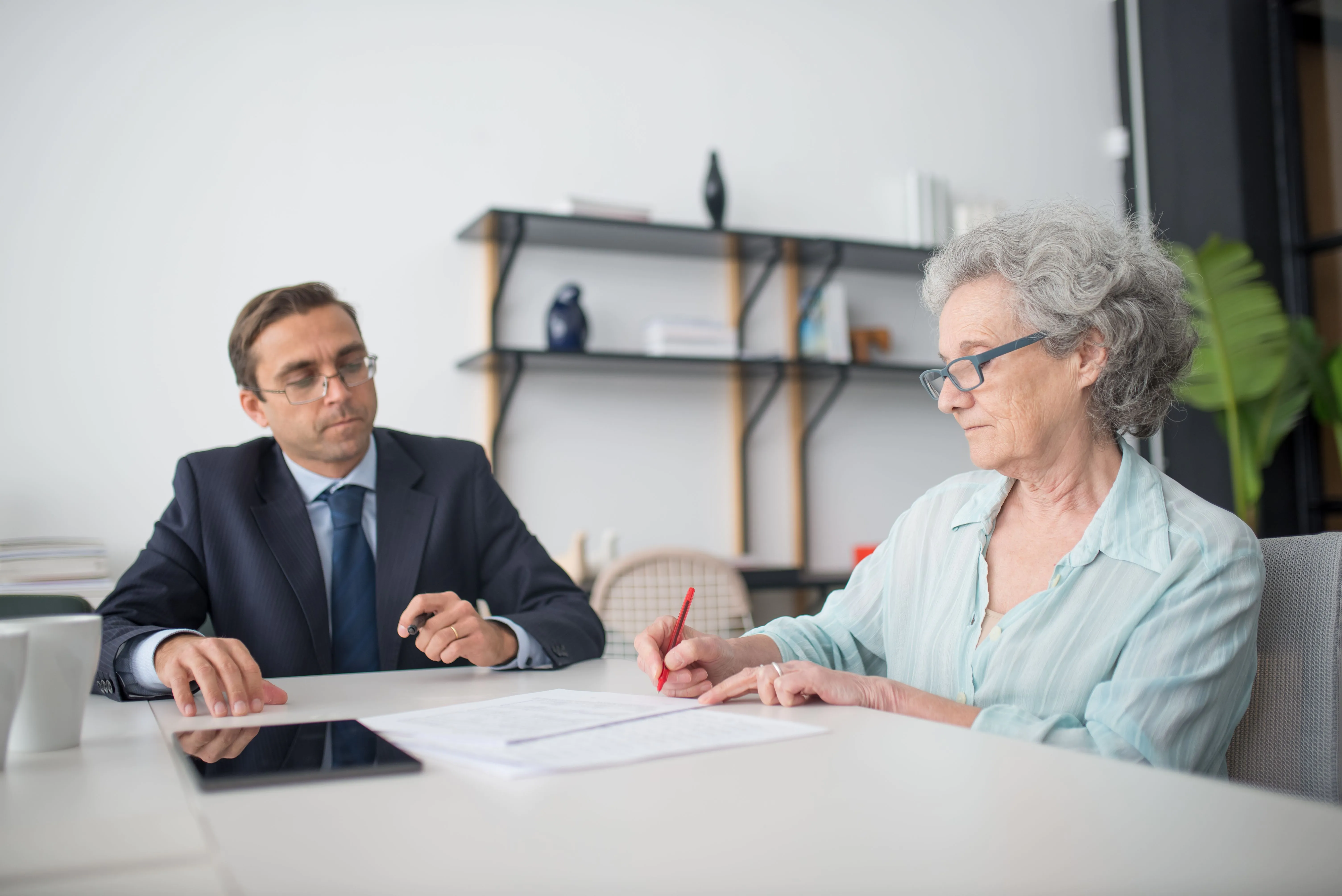 Older woman signing paperwork during a consultation, a reminder to review Medicare documents before sharing personal information.